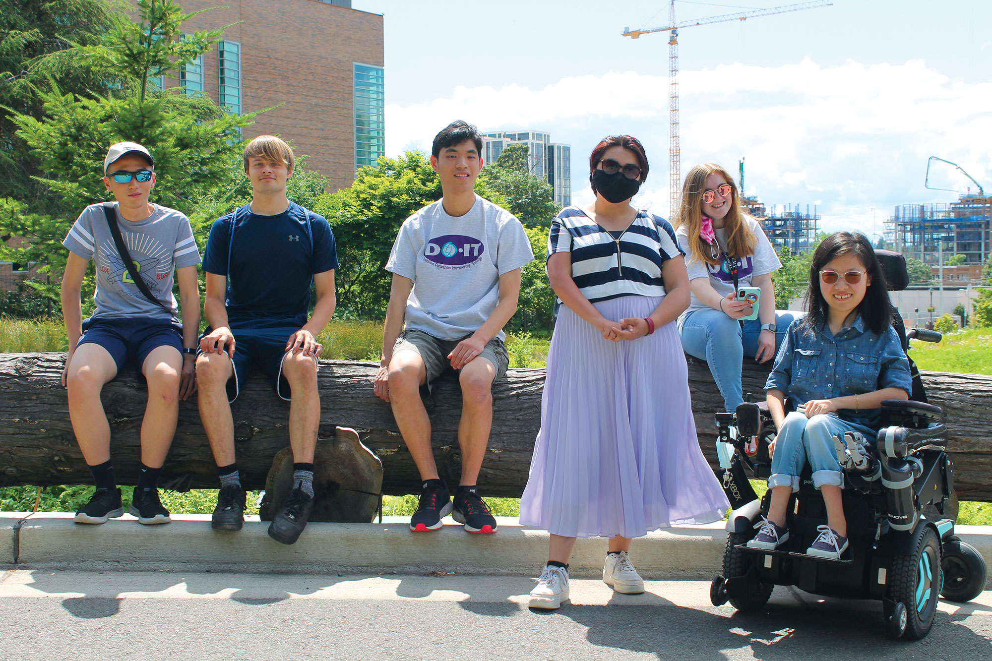 A group of young people sits and stands outside a campus building on a sunny day.