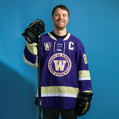 Ryan Minkoff smiles while wearing his UW Hockey Club uniform and holding a hockey stick