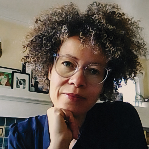 Wendy Barrington wears a dark blue shirt and clear glasses and rests her head on her chin while looking into the camera.
