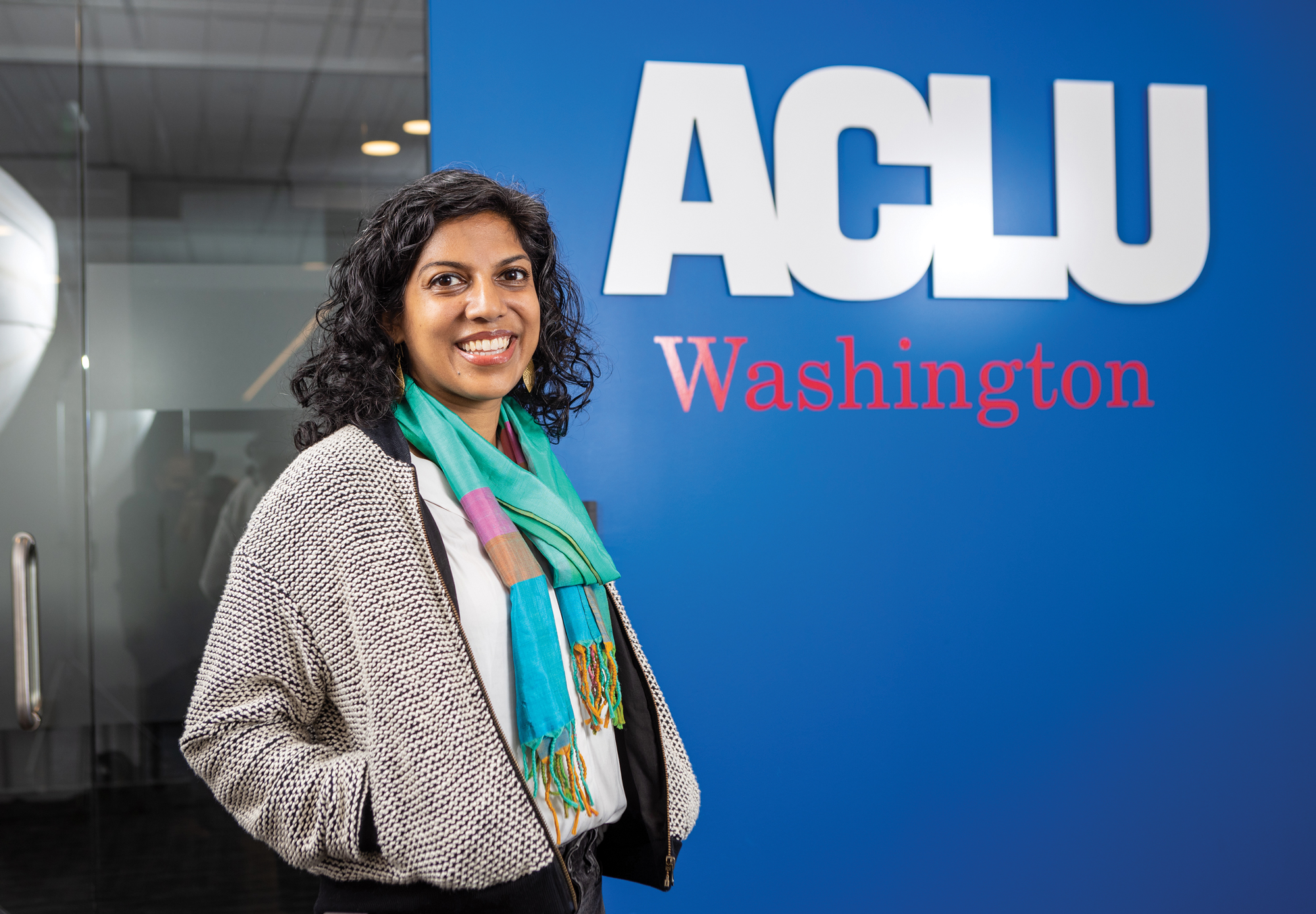A woman in formal attire stands smiling in front of a sign for ACLU Washington