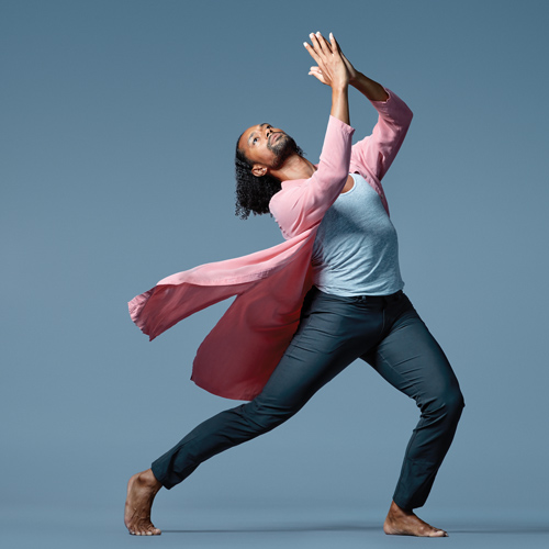 Dancer Abdiel Jacobsen poses wearing dark blue pants, a light blue tank top and a pink cardigan.