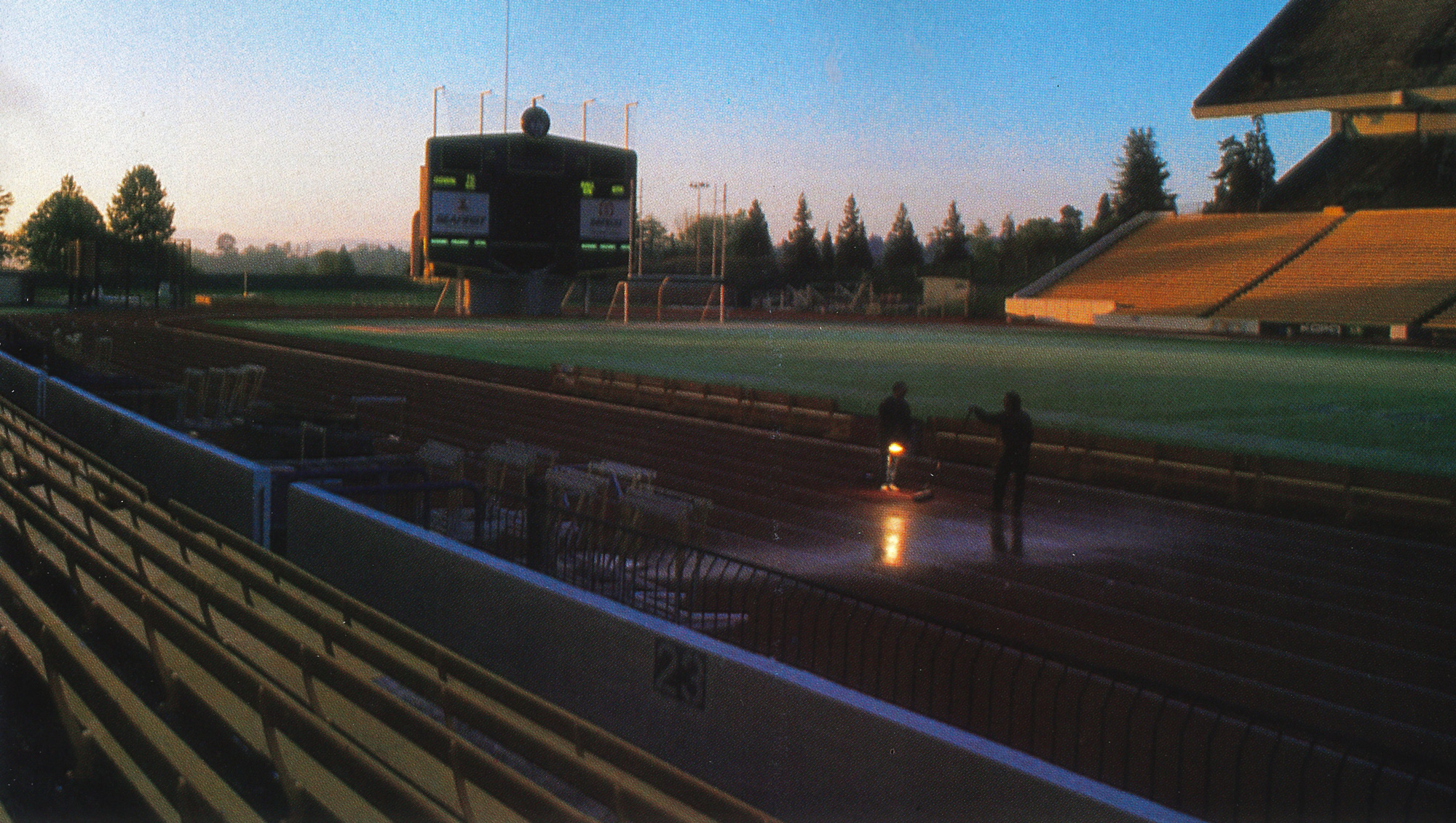 Two people shining flashlights on an athletic track early in the morning