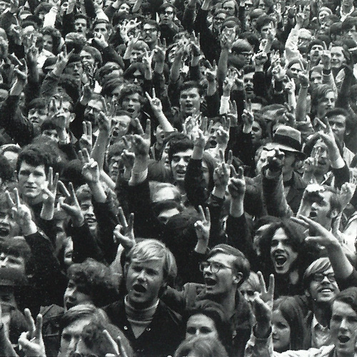 A crowd of young people holding up peace signs with their fingers