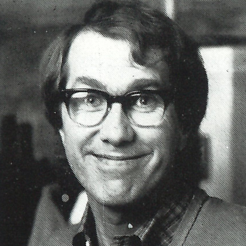Black and white film headshot of Harry Groener smiling, wearing horn rimmed glasses