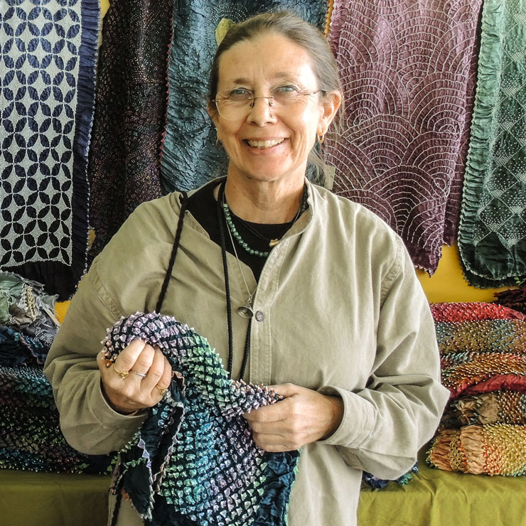 A woman stands in front of a craft booth holding fabric