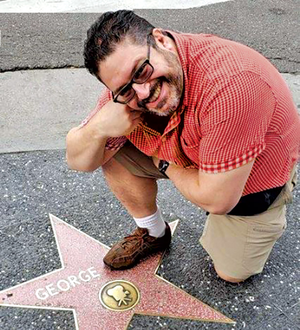 A man in a red shirt kneels near a Hollywood Walk of Fame star that says "George," but he's placing his foot over the last name.