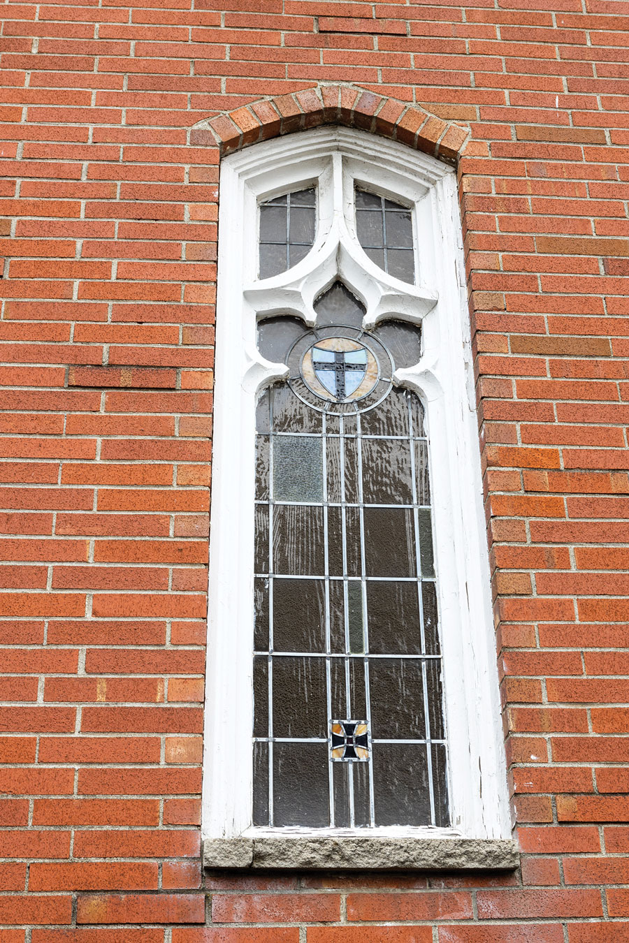 Red brick exterior with a window featuring a stained glass crucifix