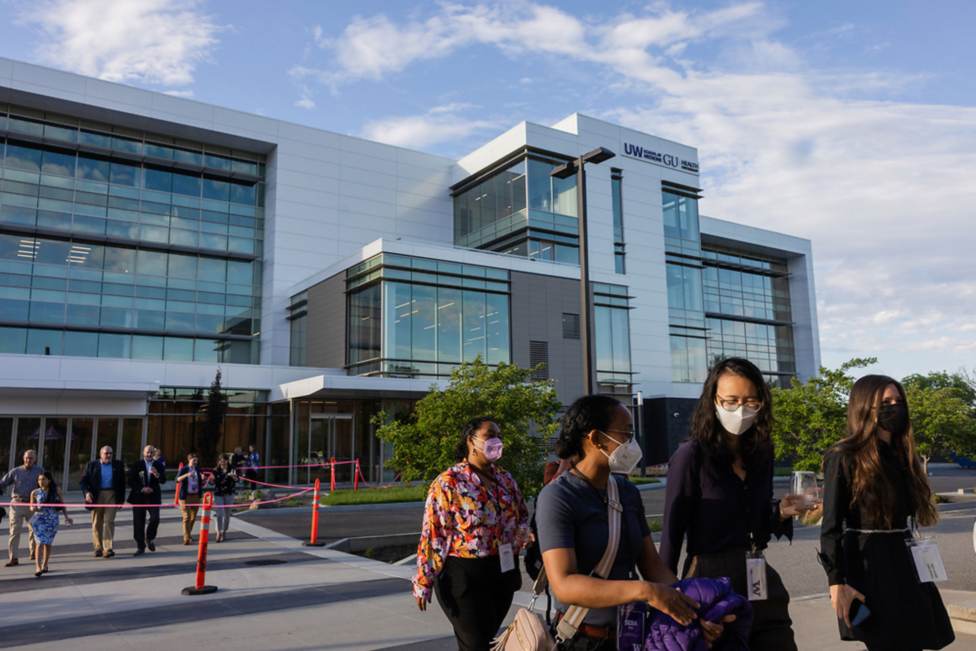 Students wearing masks walk outside a large new building on a sunny day
