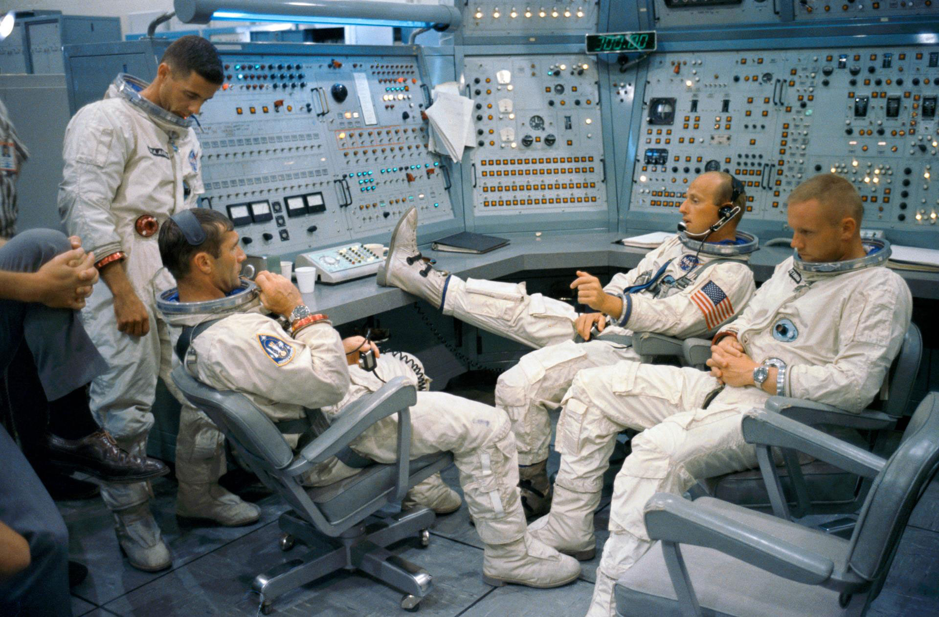 Four men in spacesuits looking relaxed in a simulator