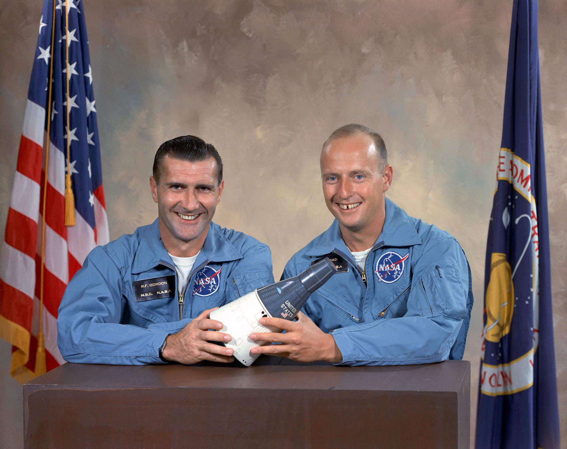 Two men pose for a photo holding a small spacecraft replica