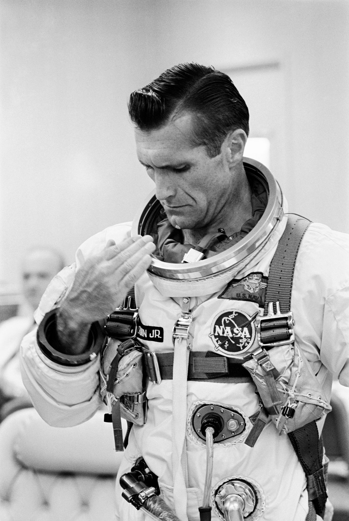 A black and white photograph shows a man inspecting his space suit