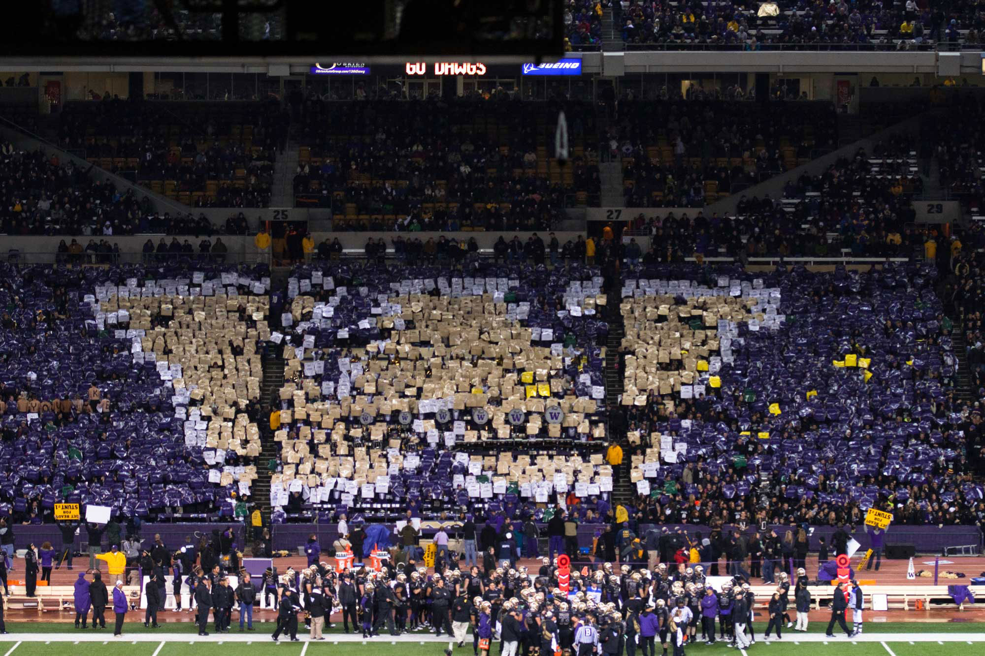 Fans holding individual purple and gold signs create a giant W in the football field stands