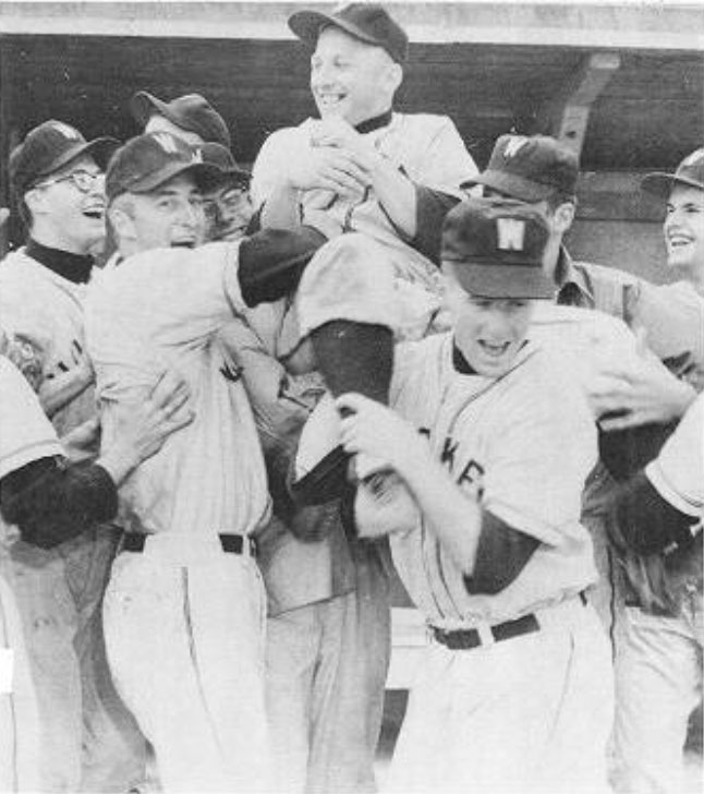 An old black and white photograph shows a smiling baseball team hoisting a fellow teammate on their shoulders