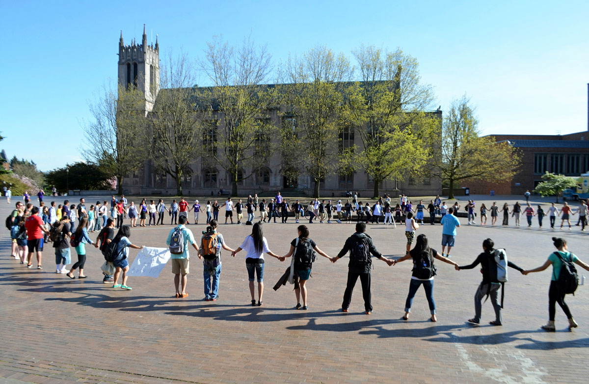A group of students stands holding hands in a circle on Red Square on the UW campus