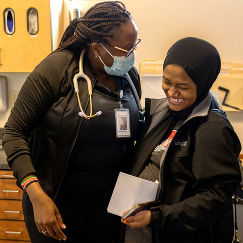 A woman wearing a surgical mask and stethoscope smiles at a laughing patient.