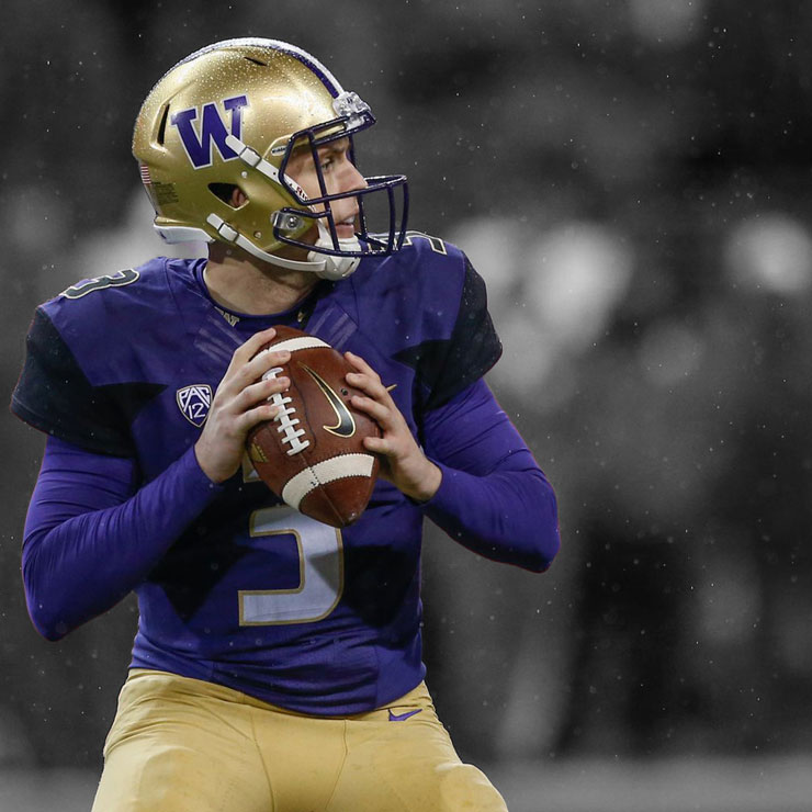 A man wearing a purple and gold uniform holding a football in the rain.