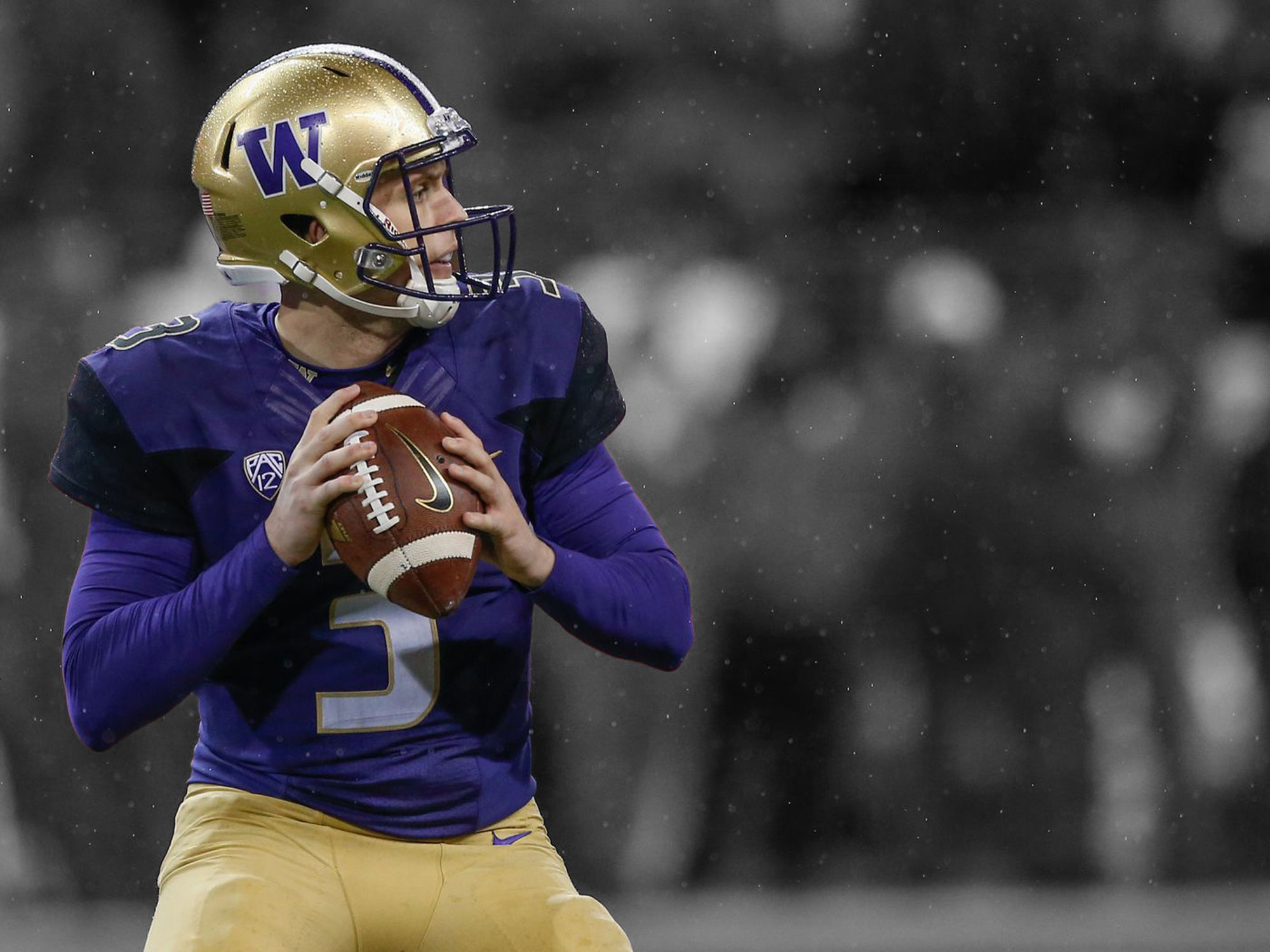 A man wearing a purple and gold uniform holding a football in the rain.