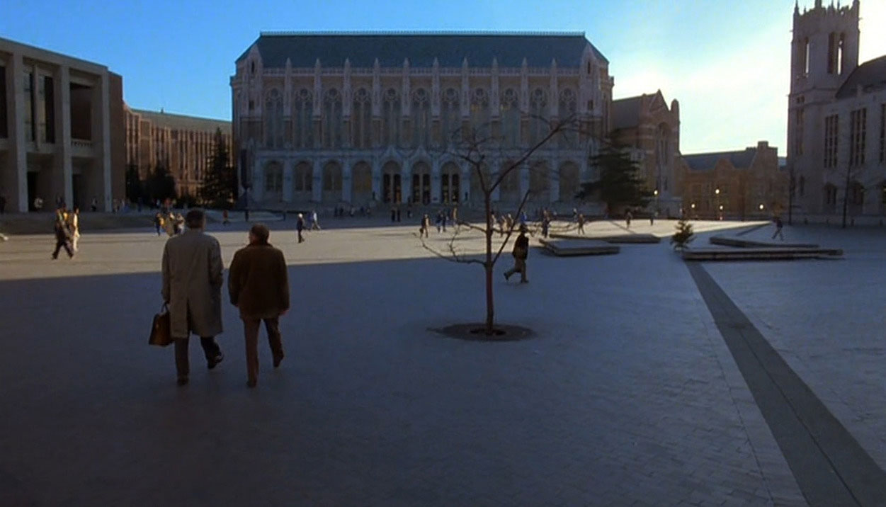 Two men walk through shadows on a college campus