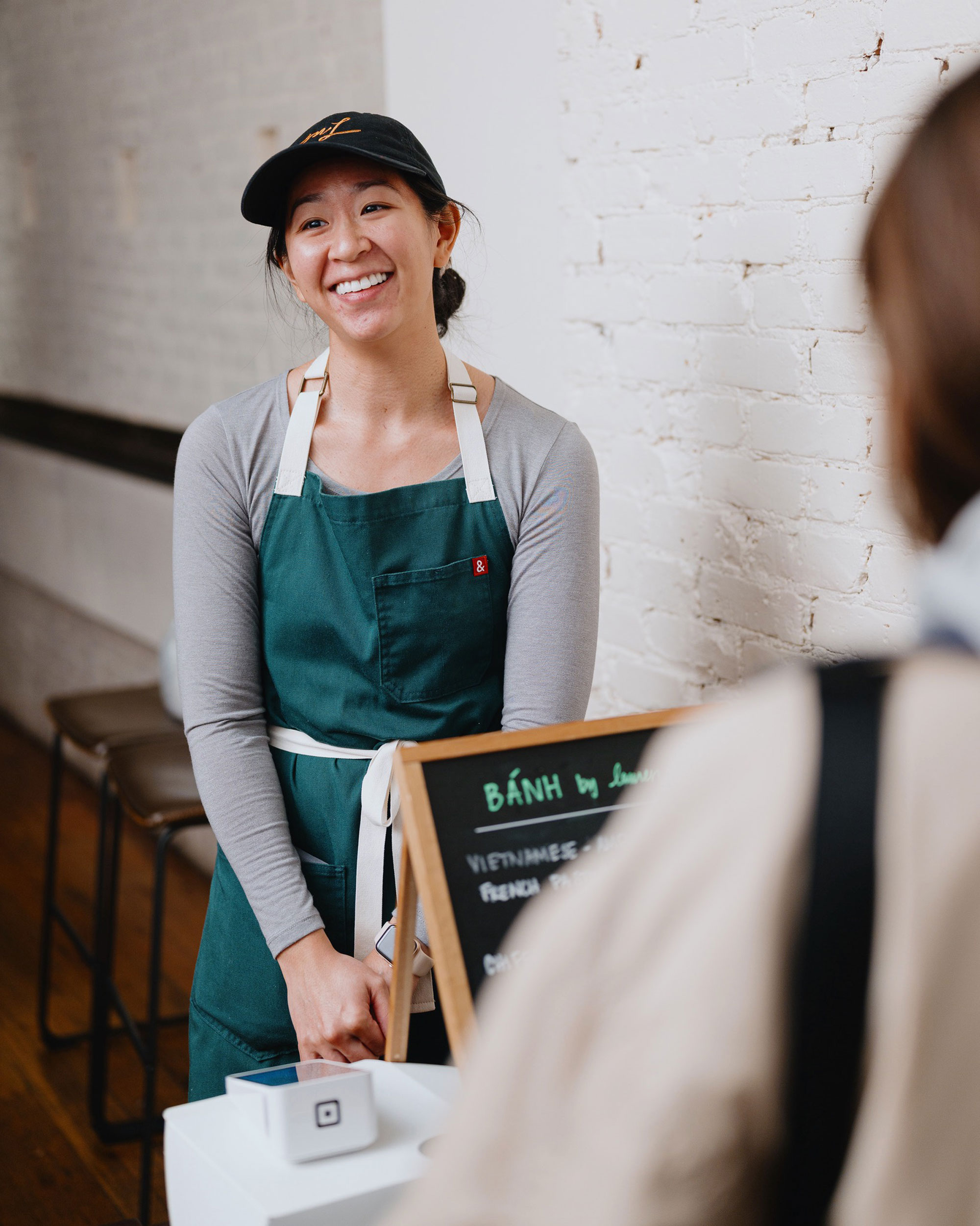 A woman in a green apron smiles at a customer