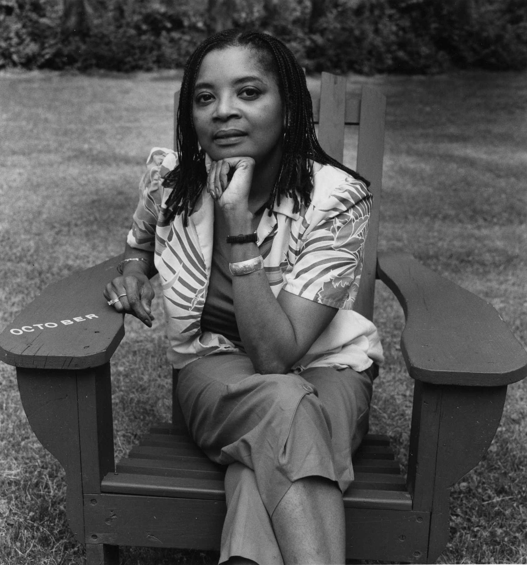 A Black woman sits in an Adirondack chair with her chin resting on a fist.