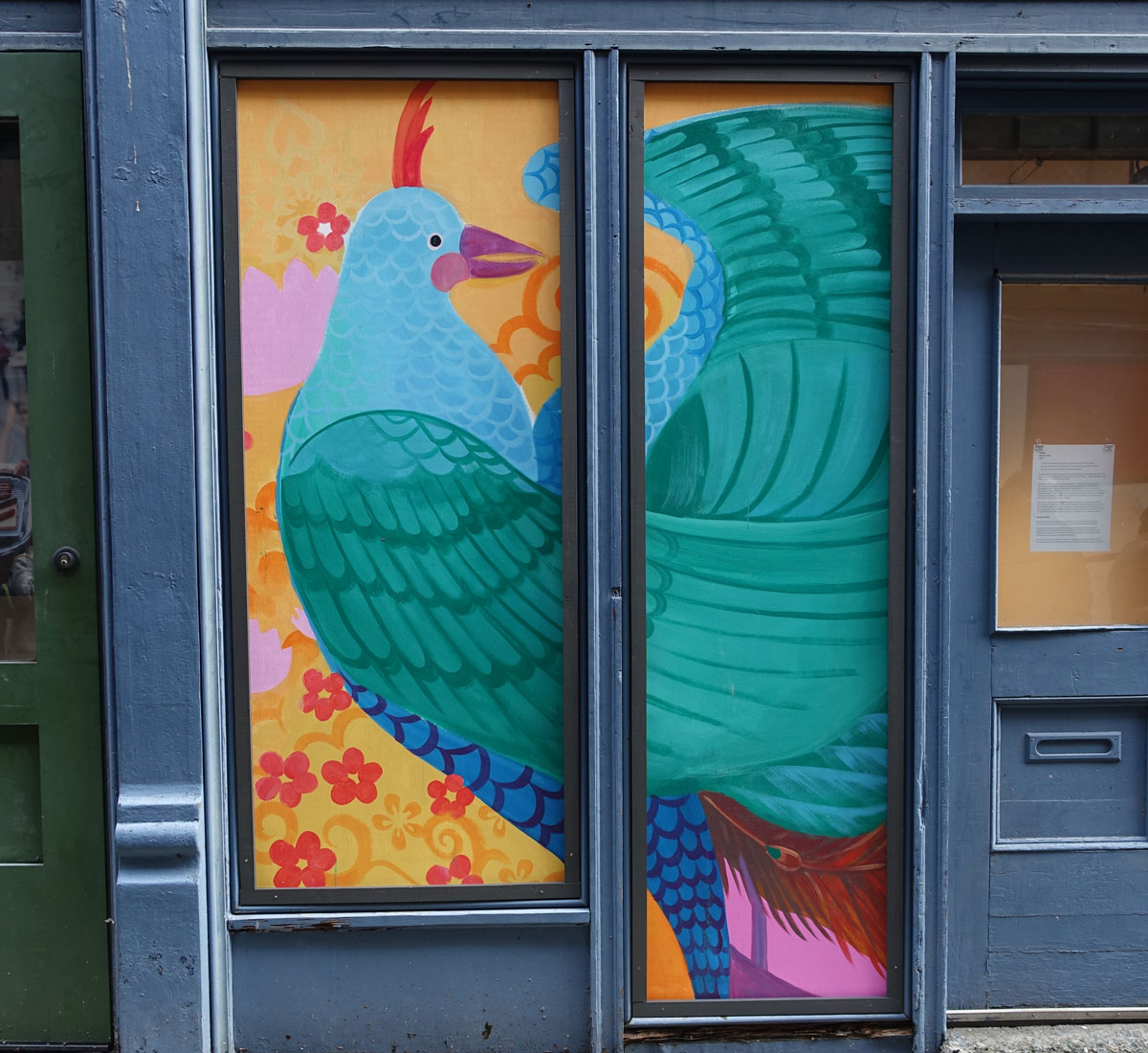 A colorful mural of a pheasant fills two windows of a city building.