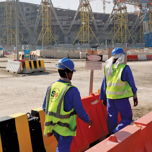 Four men in construction uniforms walk near a large stadium construction site