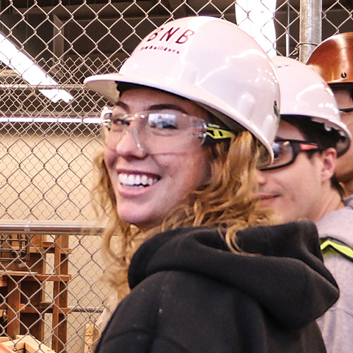A student wearing a hard hat and safety goggles smiles