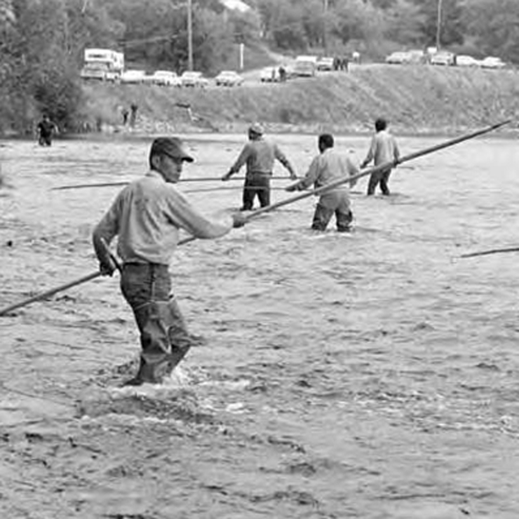 A group of men holding long fishing poles wade in a large body of water