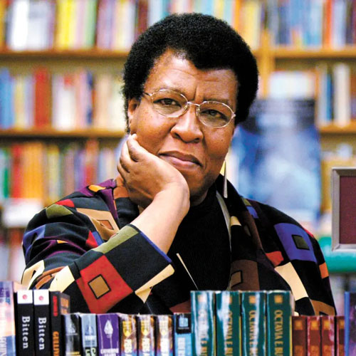 Octavia Butler poses in the book store with her elbow on a stack of her own books and her chin in her hand.