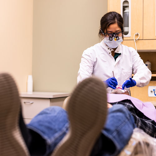 A woman wearing dentist gear works on a patient lying down