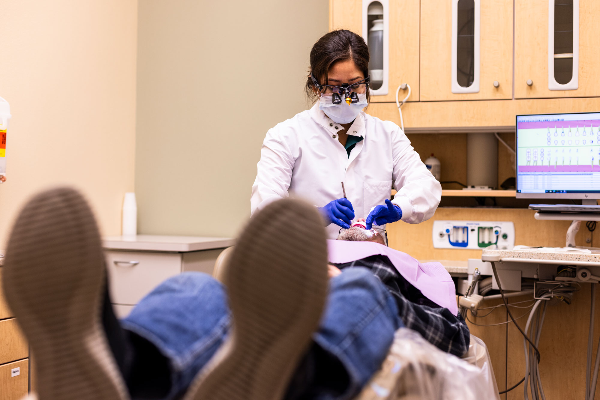 A woman wearing dentist gear works on a patient lying down