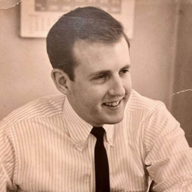 A scan of an old photograph shows a young Don Pember in a white shirt and black tie, smiling and leaning casually against his desk.