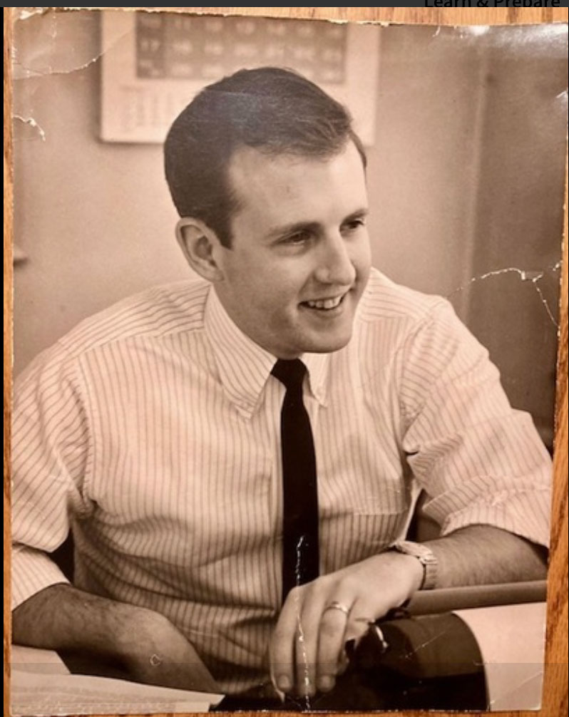 A scan of an old photograph shows a young Don Pember in a white shirt and black tie, smiling and leaning casually against his desk.