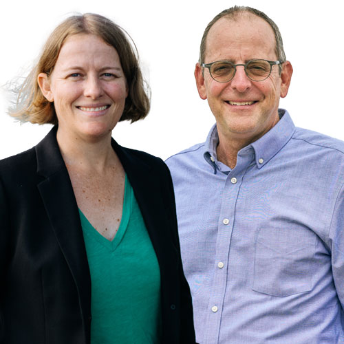 A woman in a green blouse and a black blazer stands near a man in a blue button-up shirt; both are smiling.