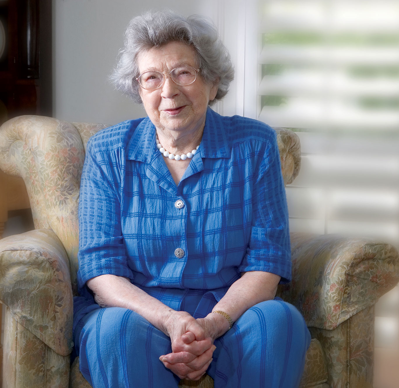 An elderly Beverly Clearly sits in a chair, smiling, weraing a blue pantsuit.