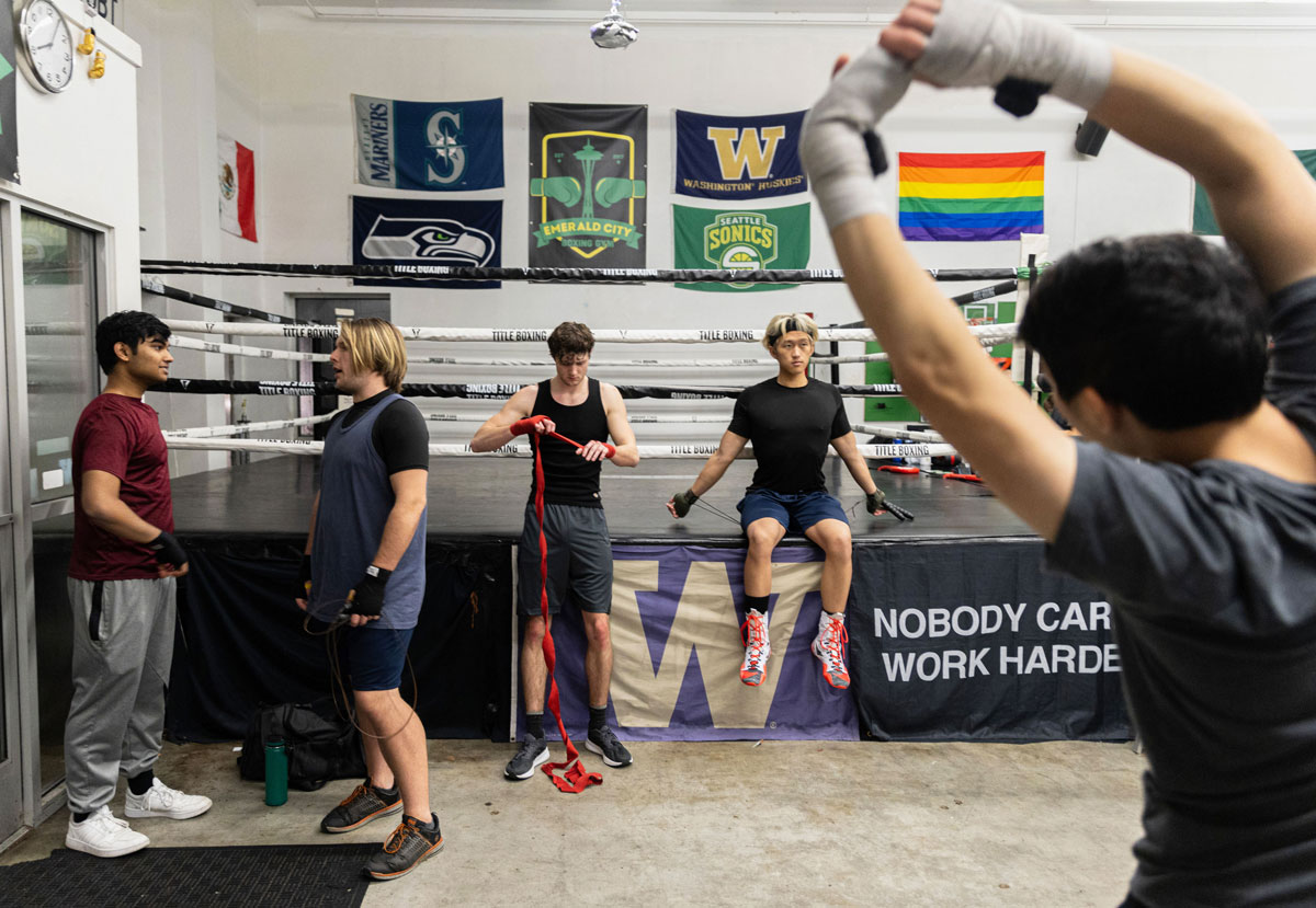 Several young men stretch and chat in a boxing gym.