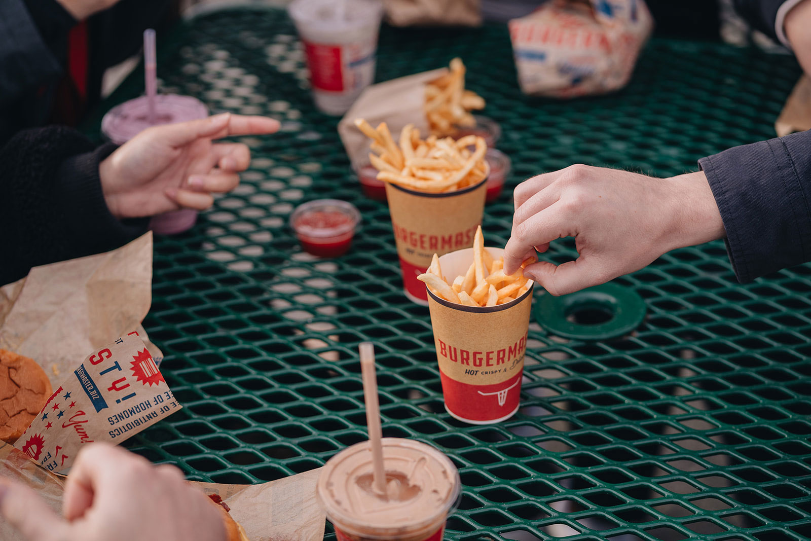 People eat from cups of fries and ketchup in the center of an outdoor seating area at Burgermaster.