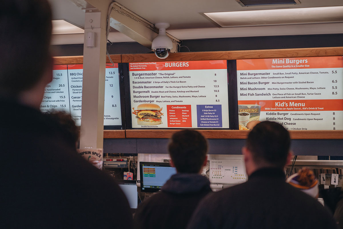 Customers wait in line and look at a menu on a TV screen inside Burgermaster