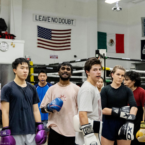 A group of tough-looking young men and women stand at ease in a boxing gym.