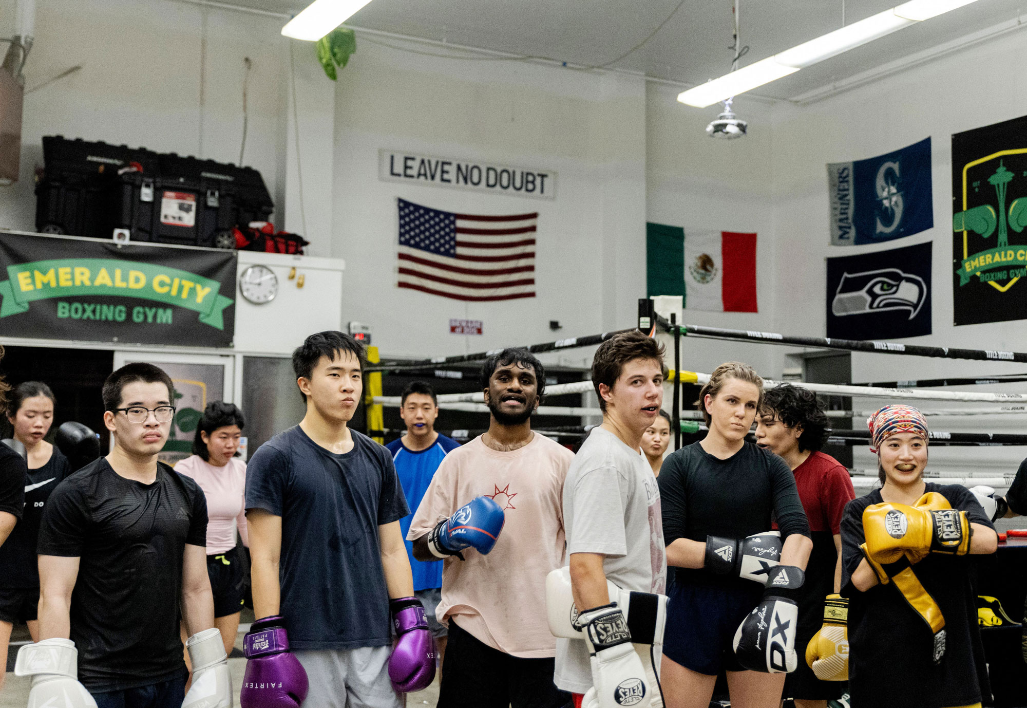 A group of tough-looking young men and women stand at ease in a boxing gym.