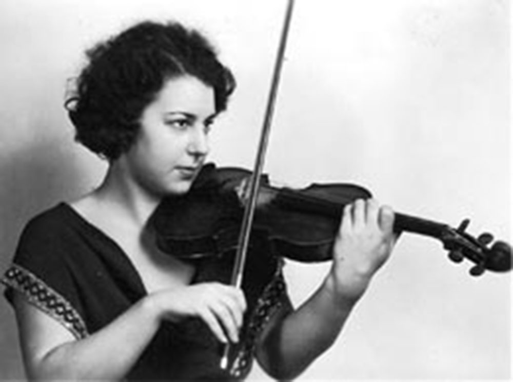 A very old photo shows a woman in a black dress playing a violin.