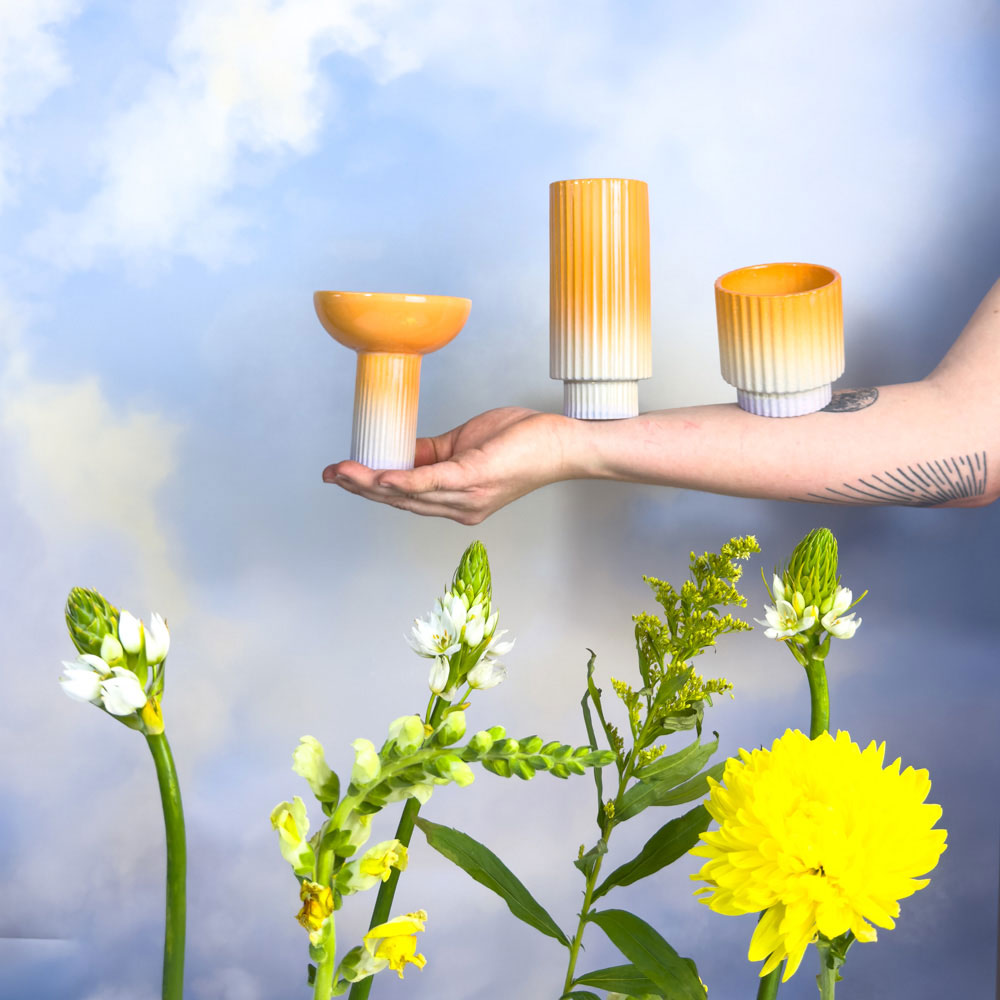 Three pieces of orange and white pottery balanced on an arm against a cloudy background