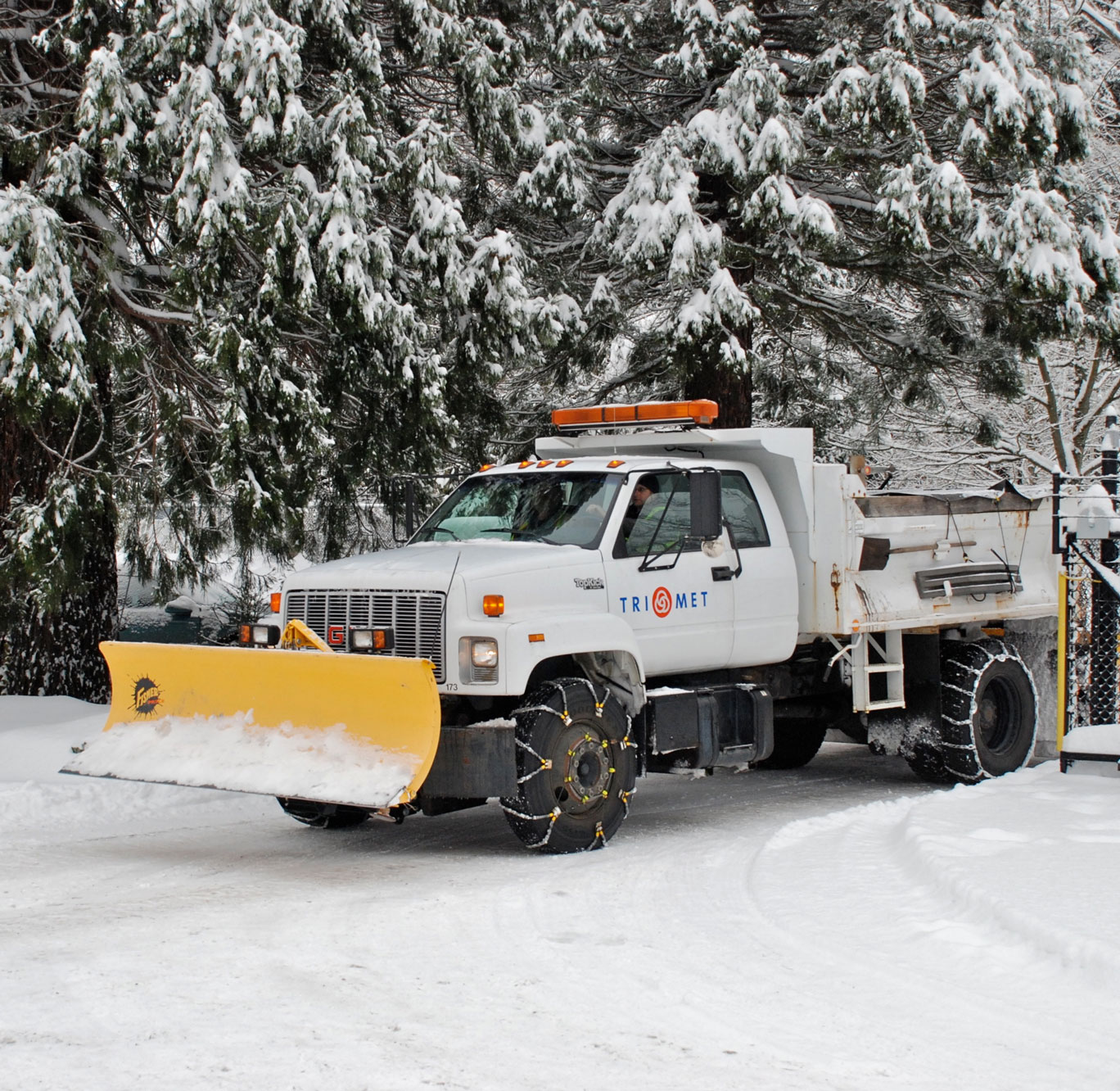 A white truck with a yellow plow at the front. The truck is labeled "TriMet"