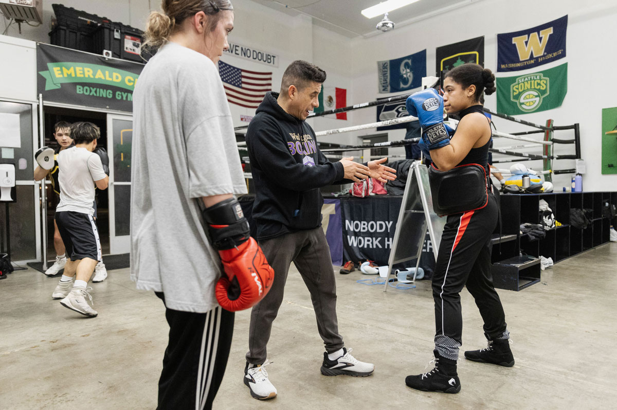 A man in a UW Boxing sweatshirt coaches a young woman in a sparring position.