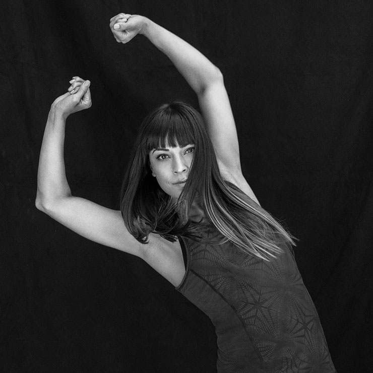 Black and white studio portrait of a woman dancing with her arms in the air