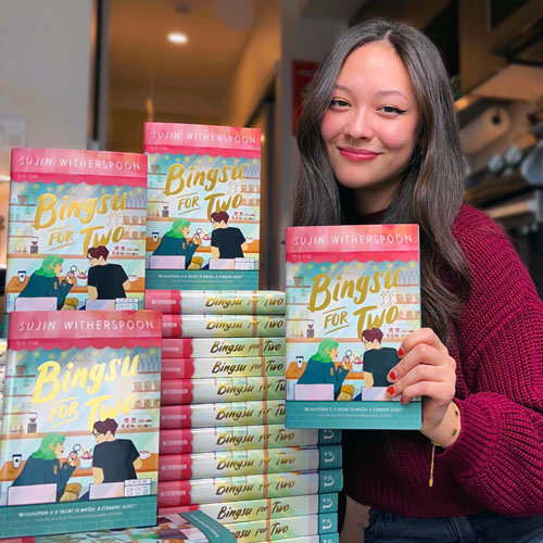 A woman poses with a stack of copies of the book that she authored