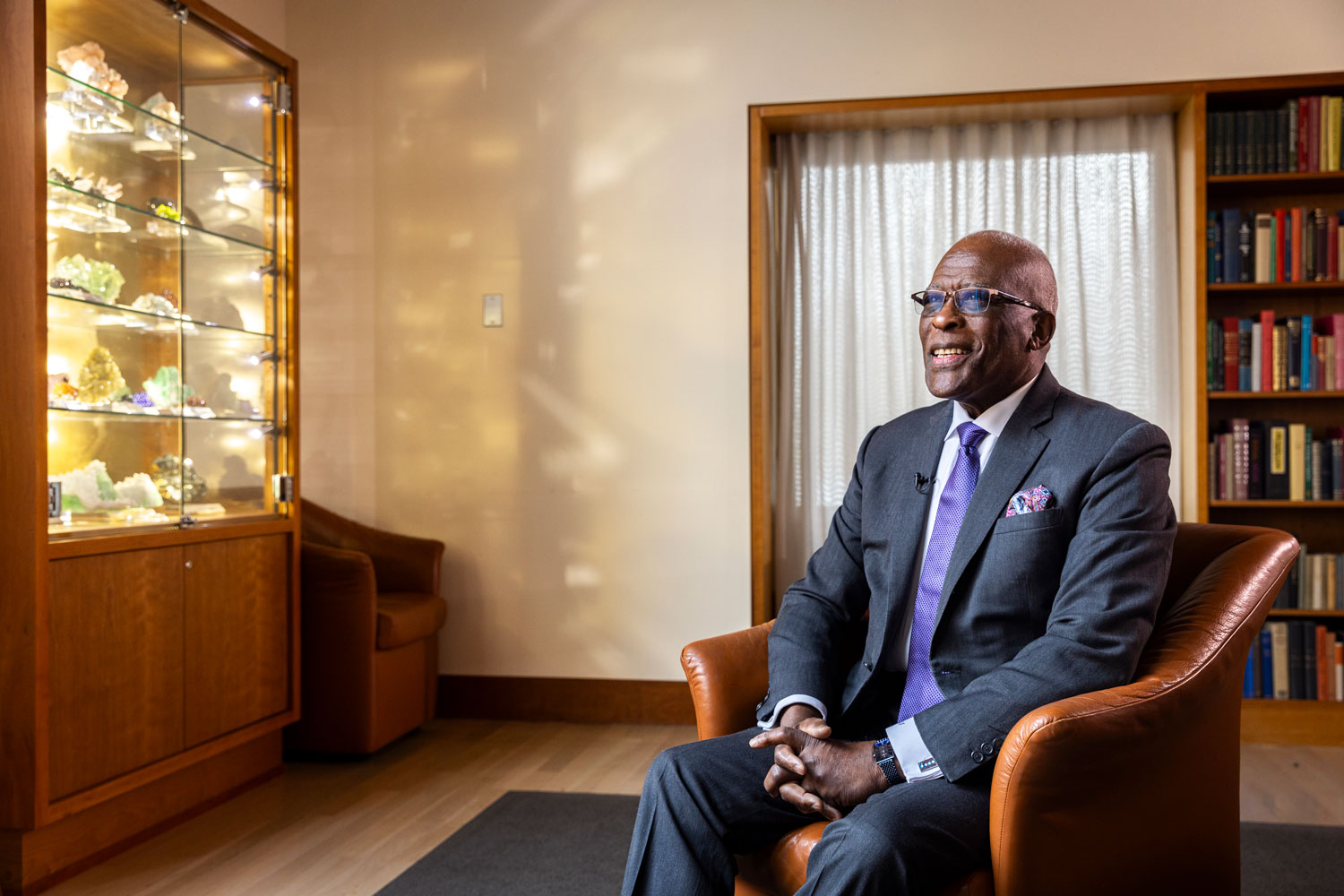 Dr. Jones, wearing a suit and purple tie, sits in a chair and smiles in an office