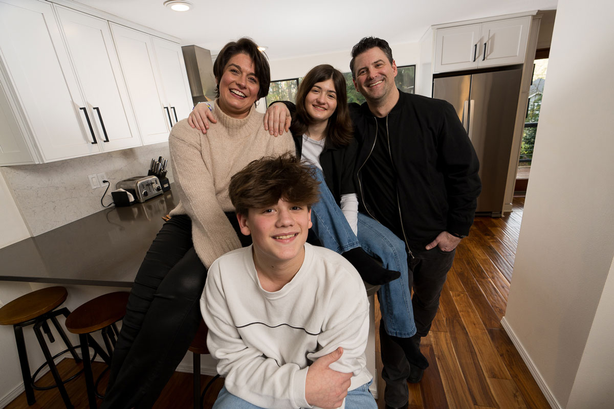 A picture of a smiling family - a mother, father, son and daughter - in their home kitchen.