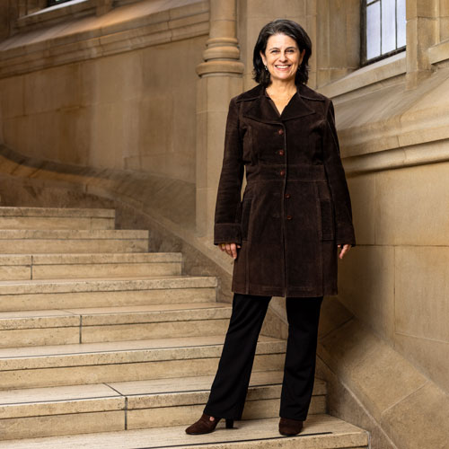 A woman in a brown corduroy jacket smiles on the steps of Suzzallo Library