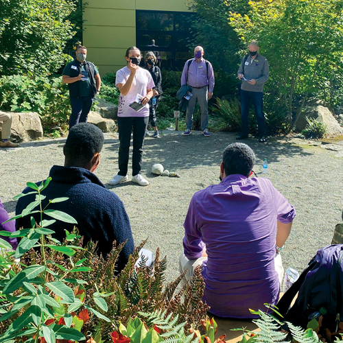 A young man gives a speech to a group of formally dressed people in an outdoor plaza